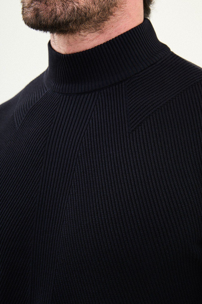 Men’s navy blue slim-fit ribbed mock-neck cotton-blend sweater with multi-directional ribbing and diagonal chest panels, styled with light gray denim.