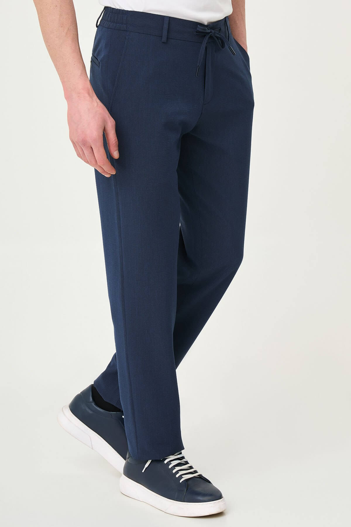 Man wearing navy blue slim-fit summer trousers paired with a white polo shirt and navy sneakers.