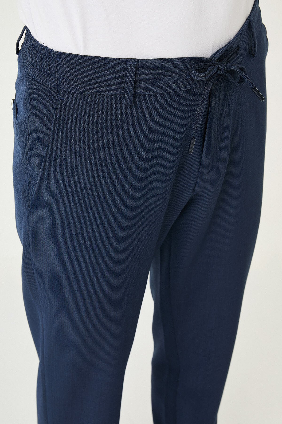 Man wearing navy blue slim-fit summer trousers paired with a white polo shirt and navy sneakers.