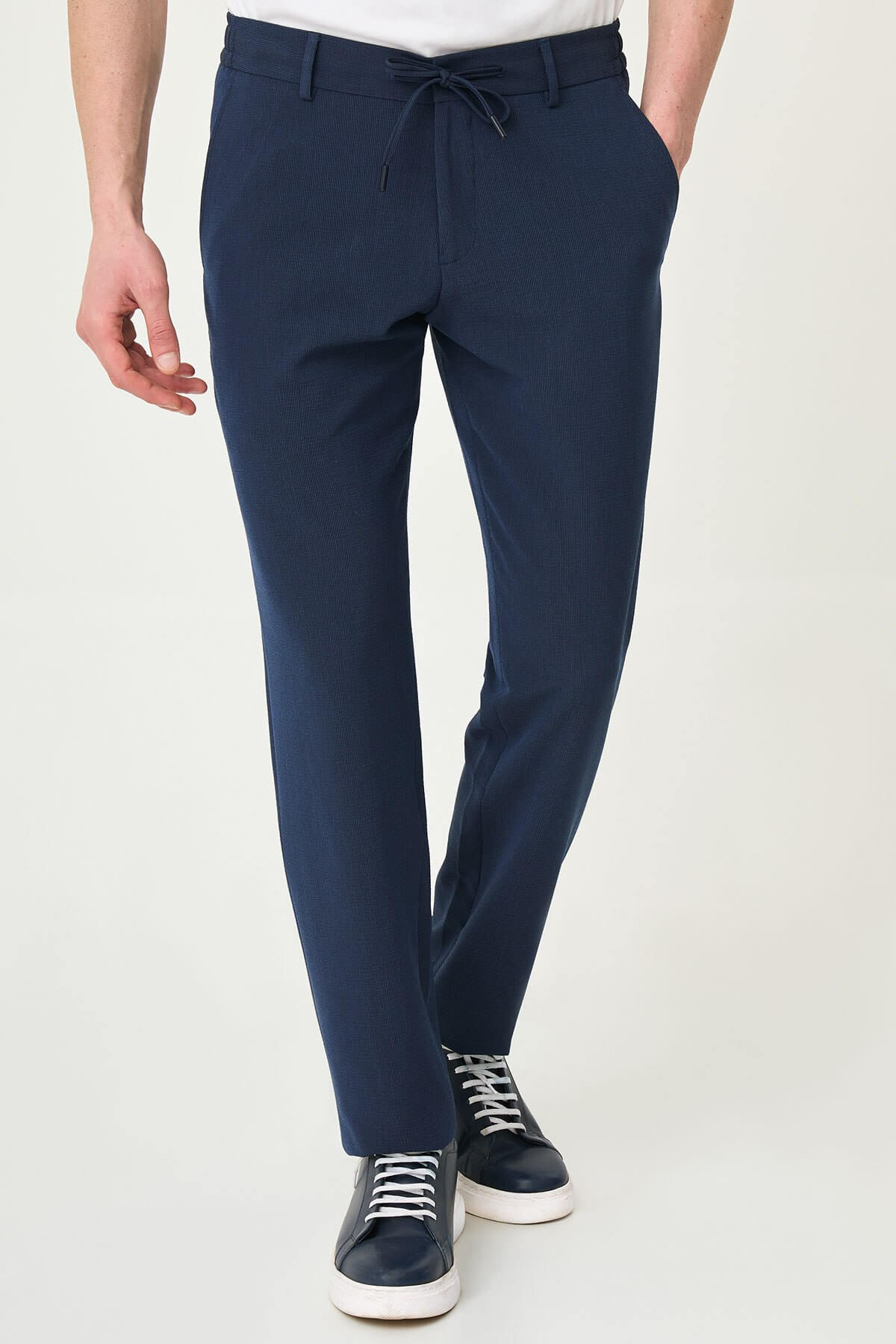 Man wearing navy blue slim-fit summer trousers paired with a white polo shirt and navy sneakers.
