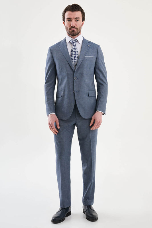 Model wearing a navy blue slim-fit three-piece suit with a white dress shirt, patterned blue tie, matching waistcoat, tailored trousers, and black leather dress shoes.