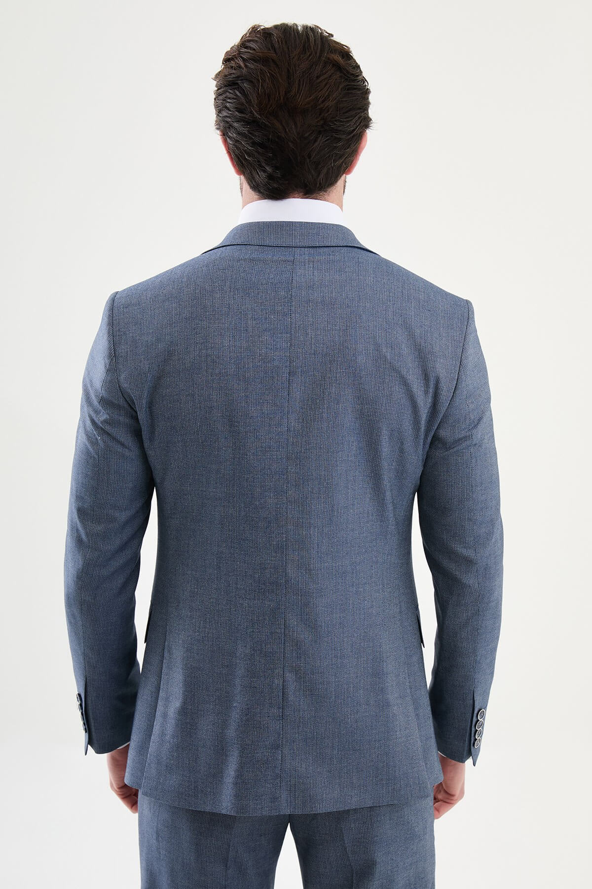 Model wearing a navy blue slim-fit three-piece suit with a white dress shirt, patterned blue tie, matching waistcoat, tailored trousers, and black leather dress shoes.