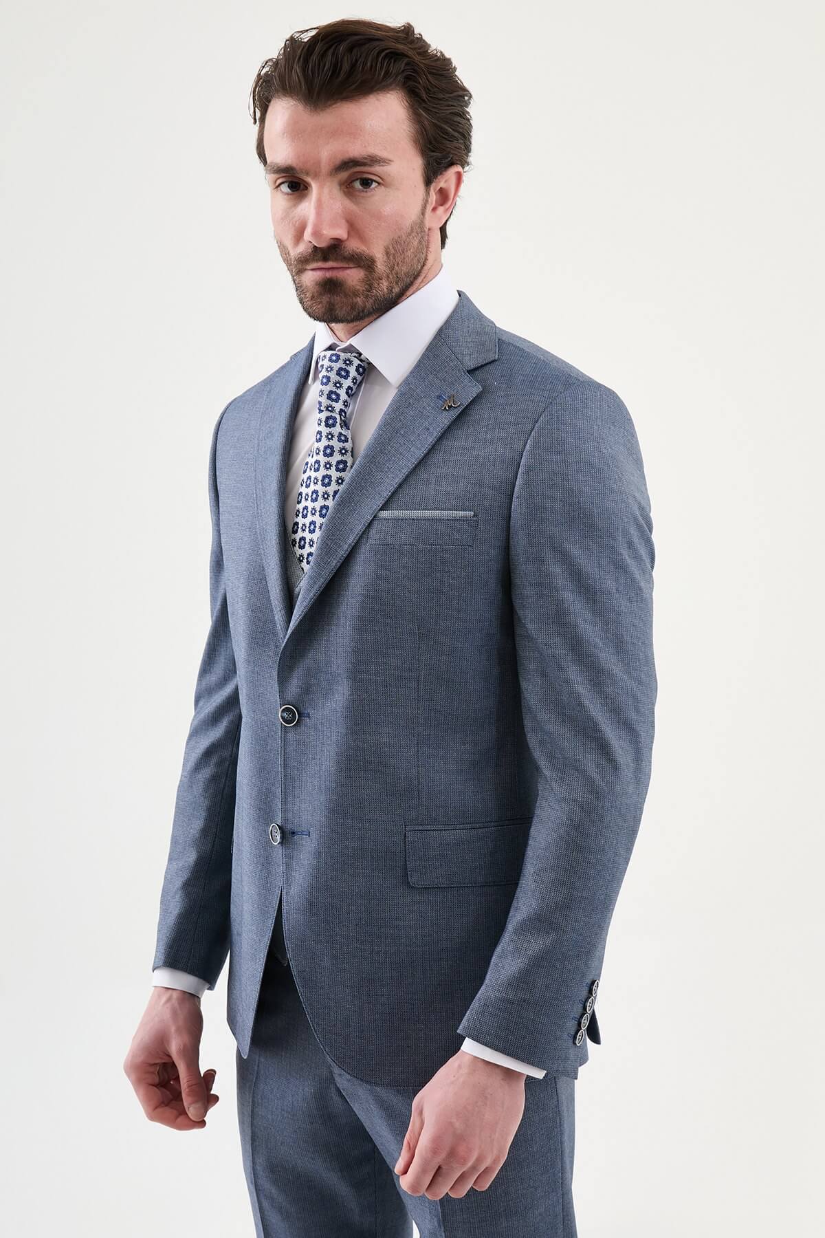 Model wearing a navy blue slim-fit three-piece suit with a white dress shirt, patterned blue tie, matching waistcoat, tailored trousers, and black leather dress shoes.