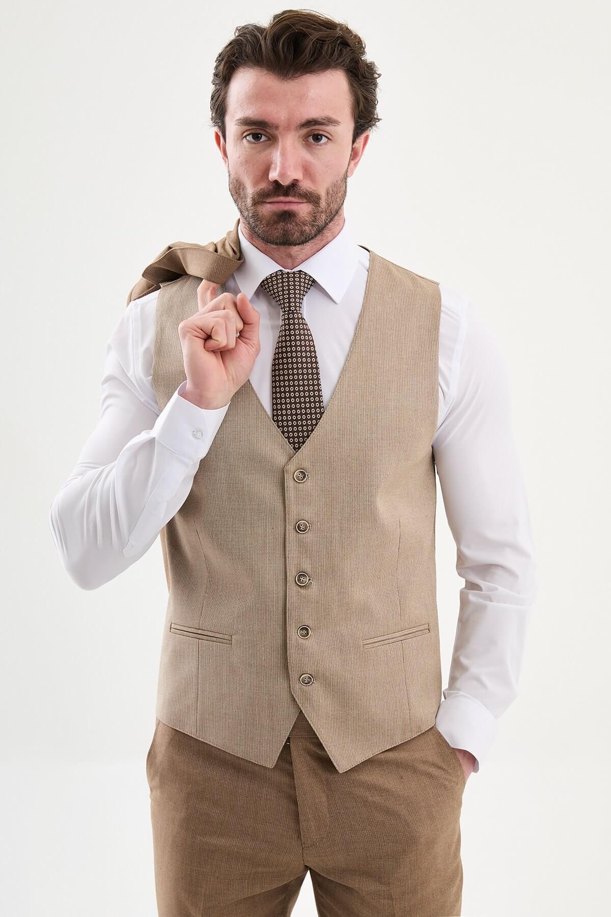 Model wearing a camel slim-fit three-piece suit with a white dress shirt, brown patterned tie, matching waistcoat, tailored trousers, and dark brown leather Derby shoes.