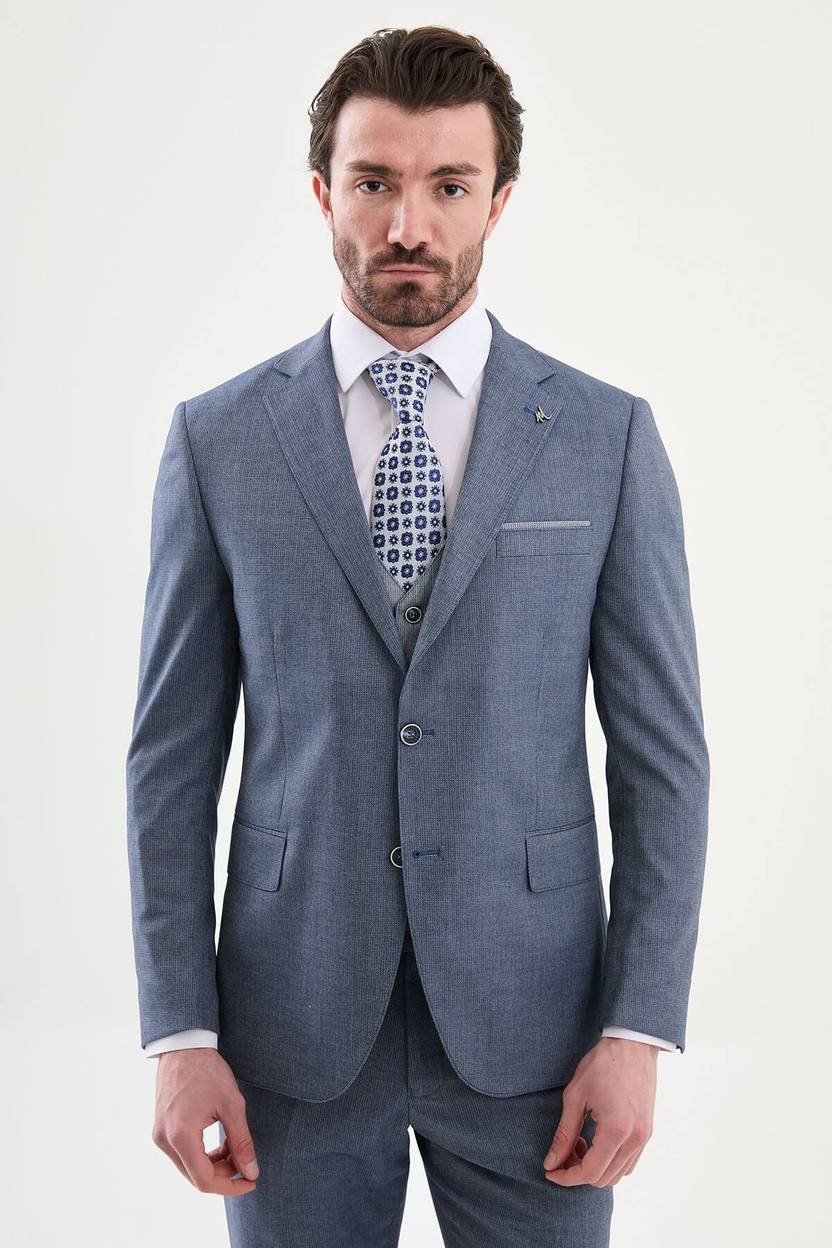 Model wearing a navy blue slim-fit three-piece suit with a white dress shirt, patterned blue tie, matching waistcoat, tailored trousers, and black leather dress shoes.