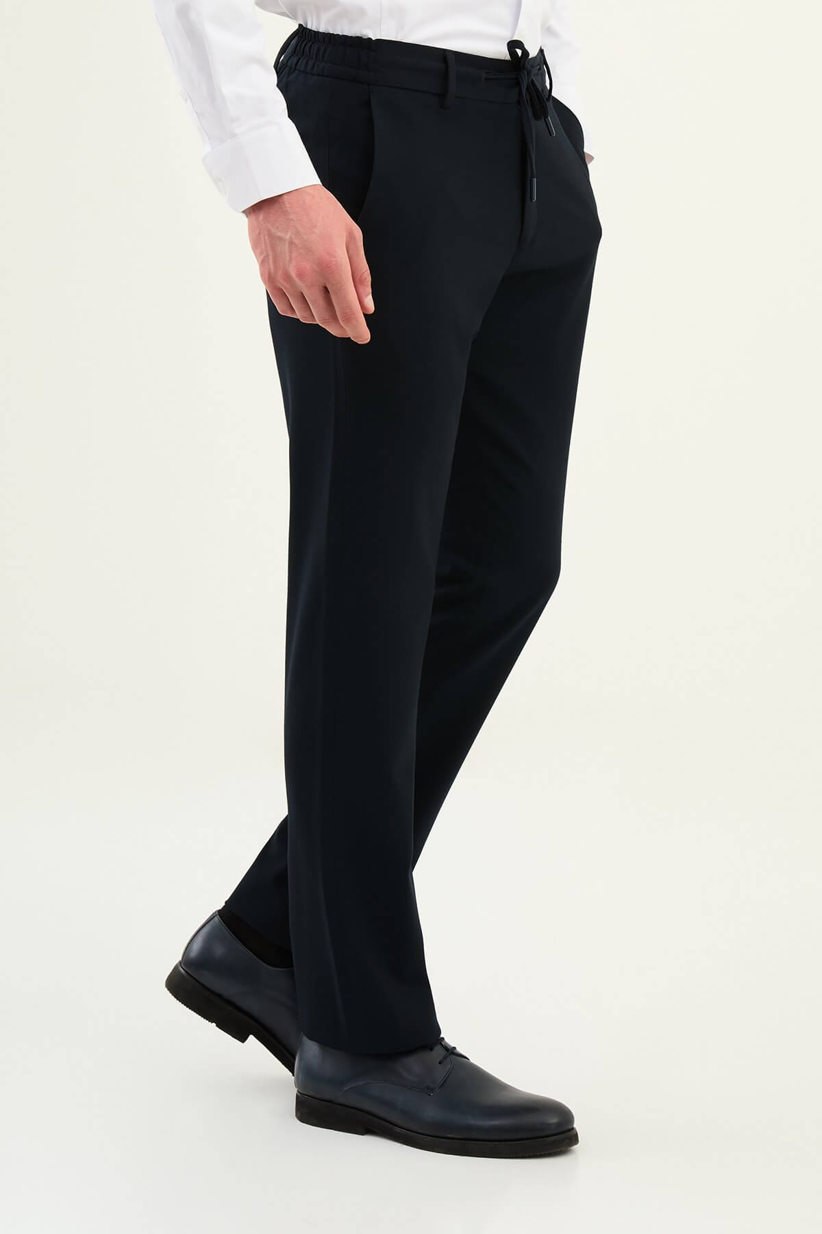 Men wearing navy blue slim-fit drawstring trousers with elastic waistband, tapered slim fit, styled with dress shoes and sneakers for versatile summer menswear.