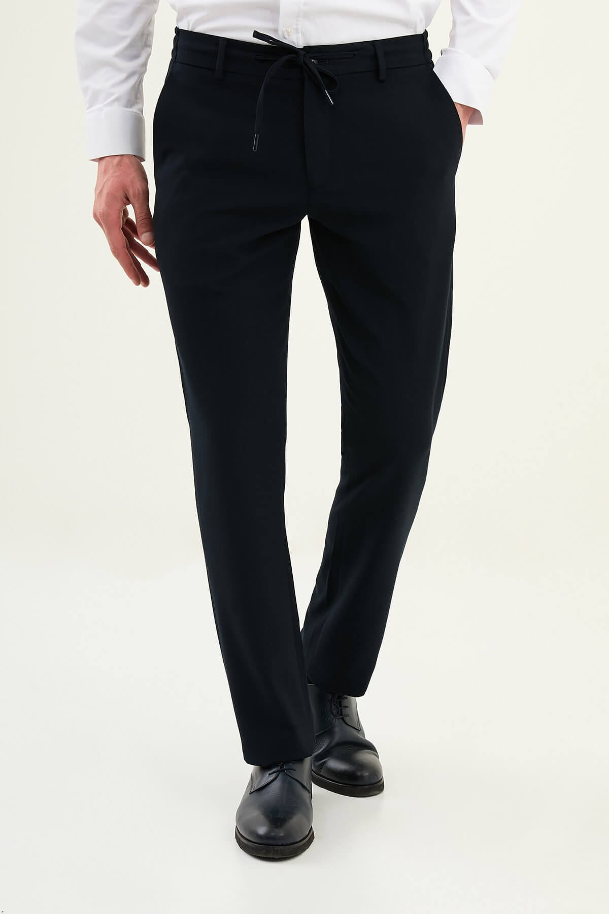 Men wearing navy blue slim-fit drawstring trousers with elastic waistband, tapered slim fit, styled with dress shoes and sneakers for versatile summer menswear.
