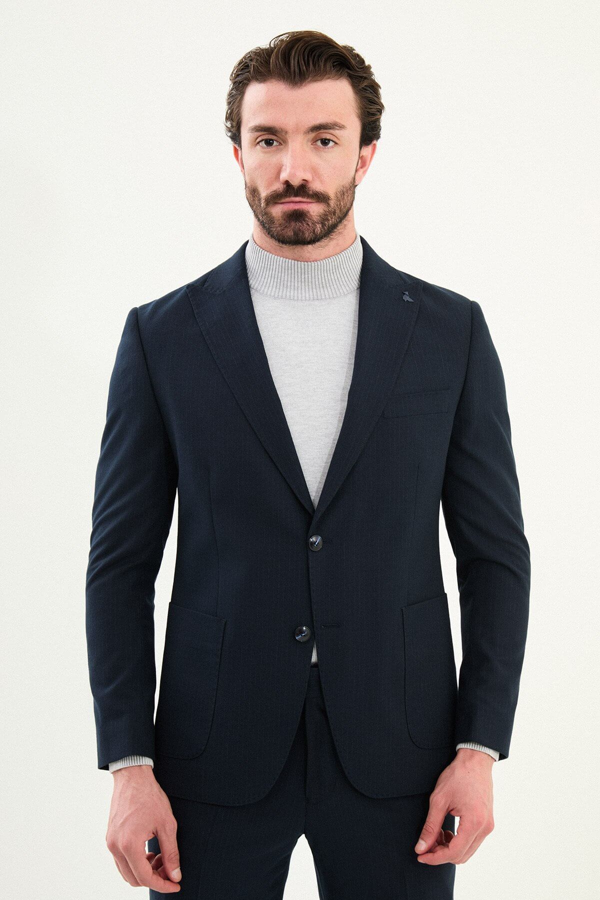 Men’s navy blue slim-fit suit with notch lapels and two-button jacket, matte micro-textured fabric, styled with a light gray mock-neck sweater for modern winter business wear.