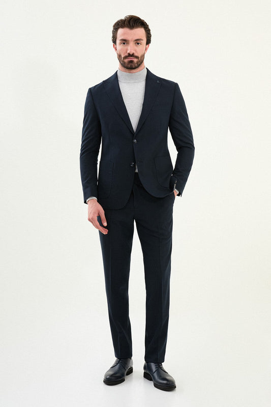 Men’s navy blue slim-fit suit with notch lapels and two-button jacket, matte micro-textured fabric, styled with a light gray mock-neck sweater for modern winter business wear.