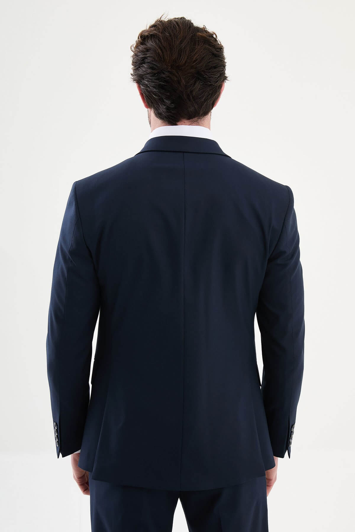 man wearing a navy blue slim-fit three-piece suit, including blazer, vest, and trousers, styled with a white shirt and tie, suitable for summer weddings and business events.