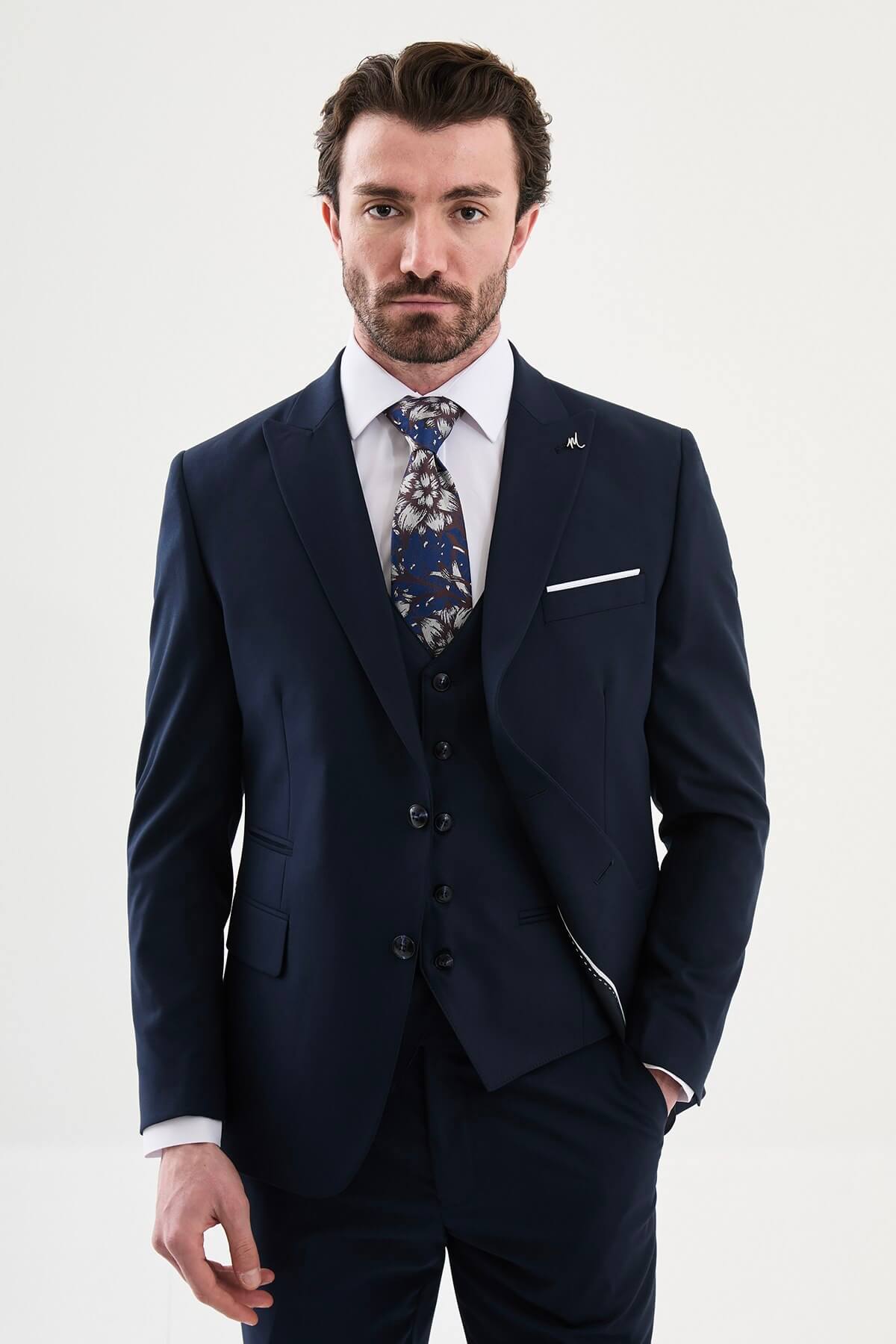man wearing a navy blue slim-fit three-piece suit, including blazer, vest, and trousers, styled with a white shirt and tie, suitable for summer weddings and business events.
