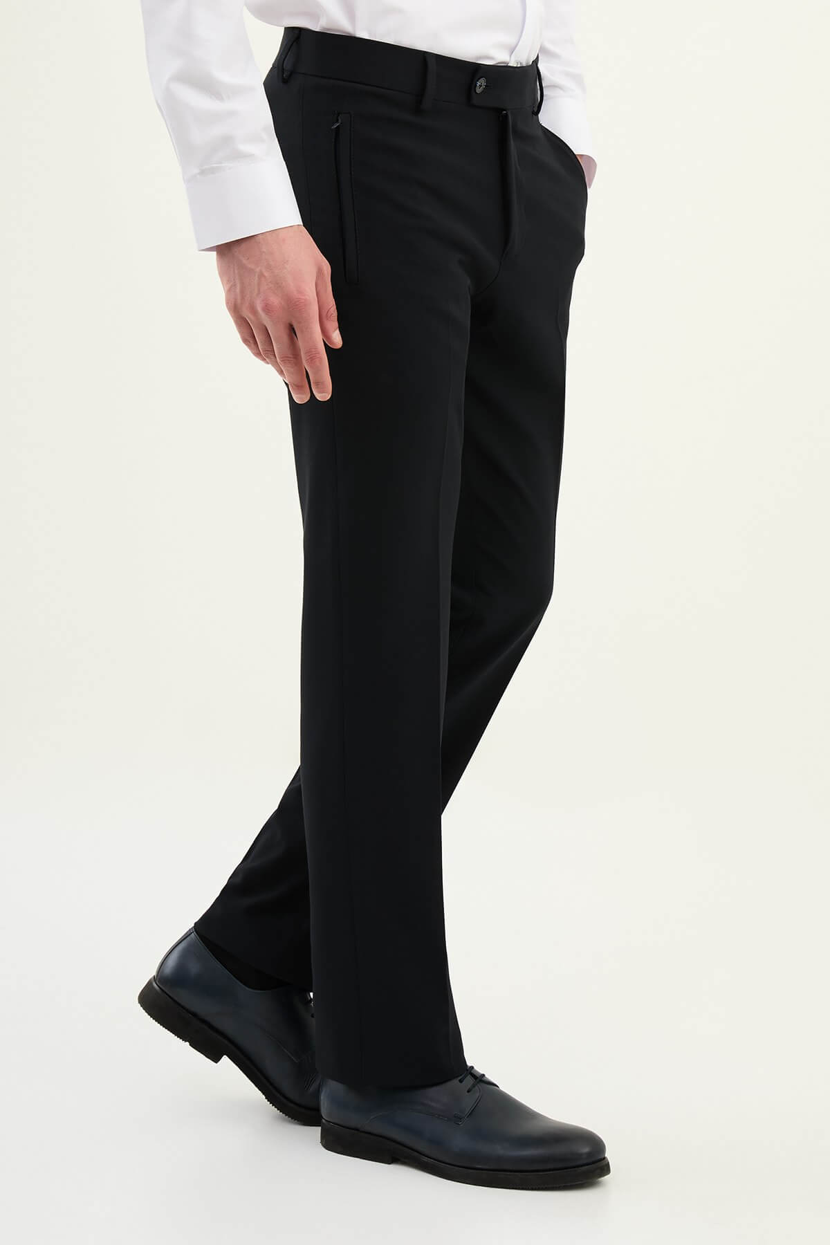 Man wearing navy blue slim-fit dress trousers styled with a white shirt and black leather shoes.
