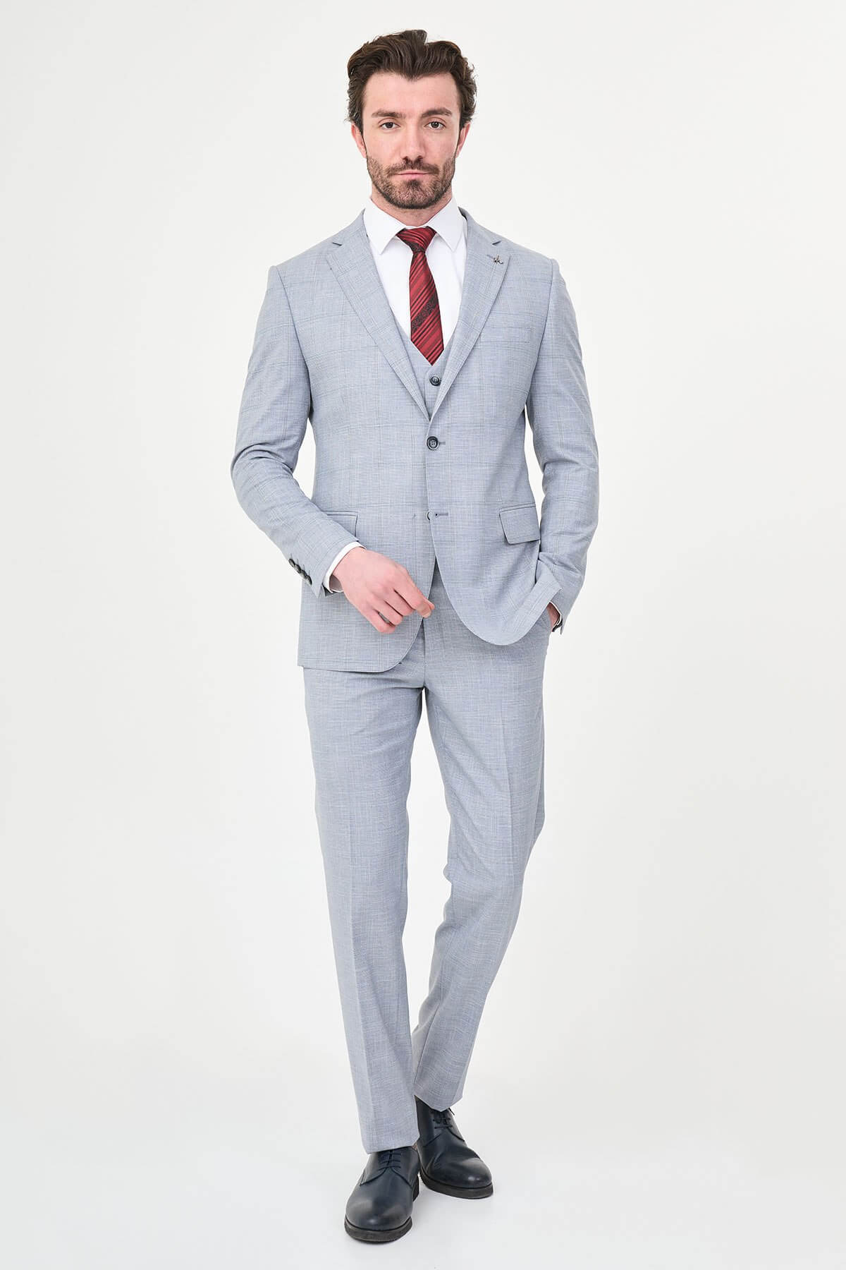a navy blue slim-fit three-piece suit with a subtle windowpane check, matching waistcoat and trousers, white dress shirt, burgundy striped tie, and black leather Derby shoes.