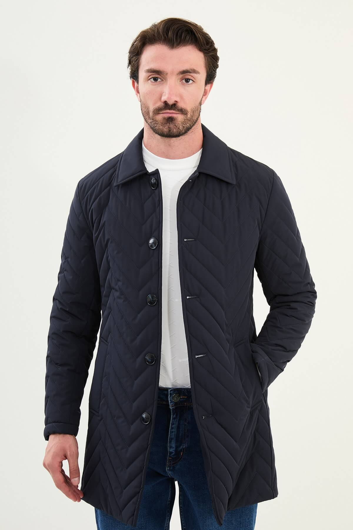 Man wearing a navy blue slim fit quilted car coat with button closure, styled with blue jeans and white sneakers.