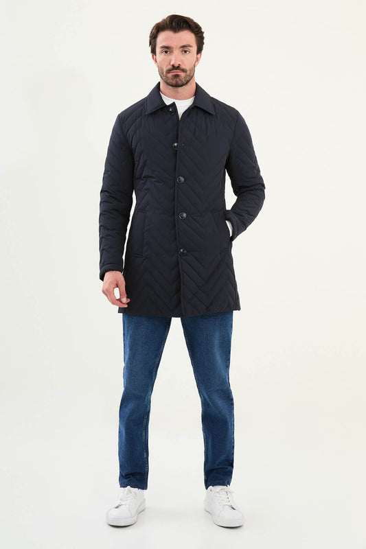 Man wearing a navy blue slim fit quilted car coat with button closure, styled with blue jeans and white sneakers.