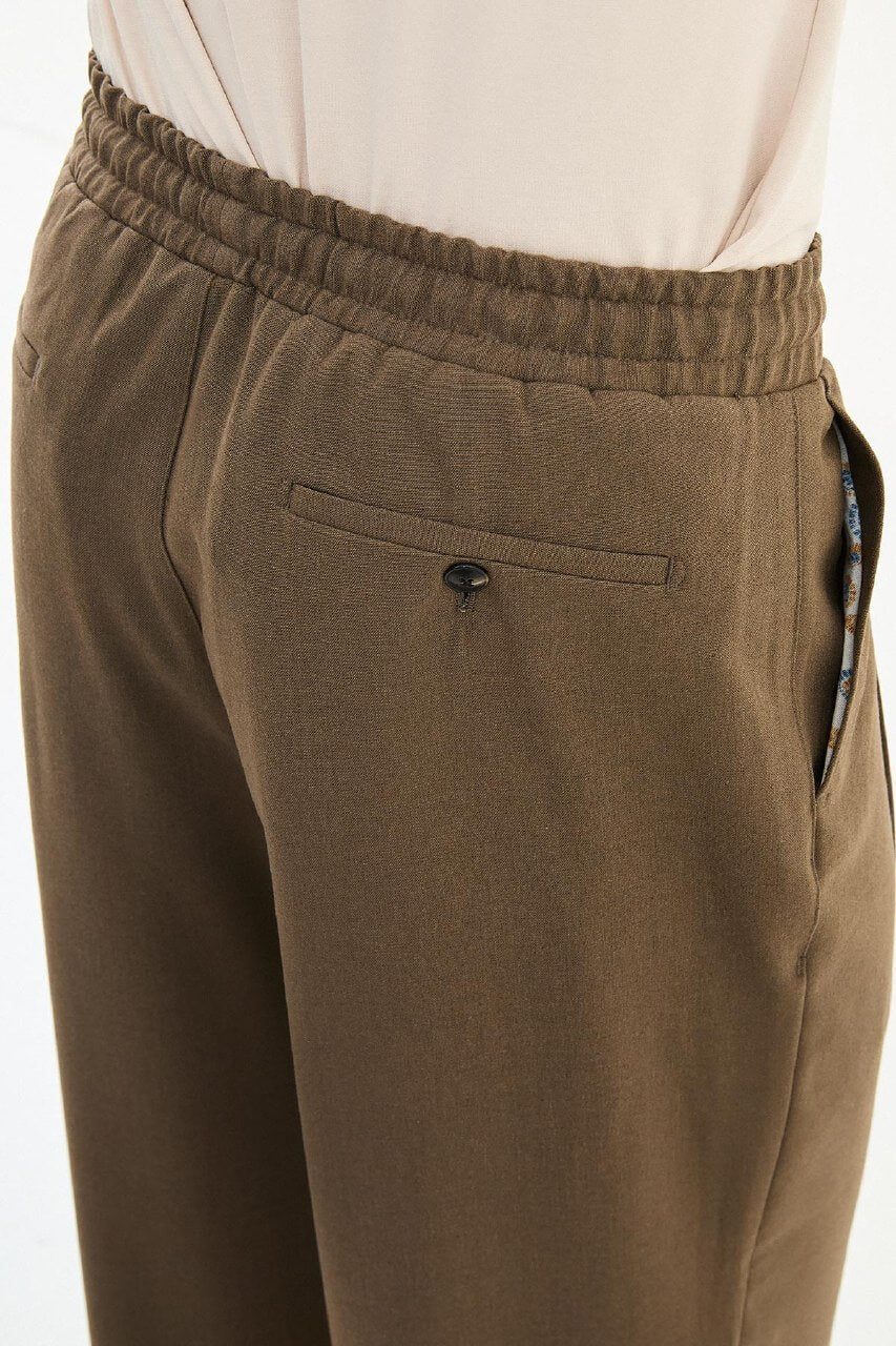 Men wearing olive brown luxe drawstring jersey pants with brown dress shoes, styled for a relaxed smart-casual summer look.