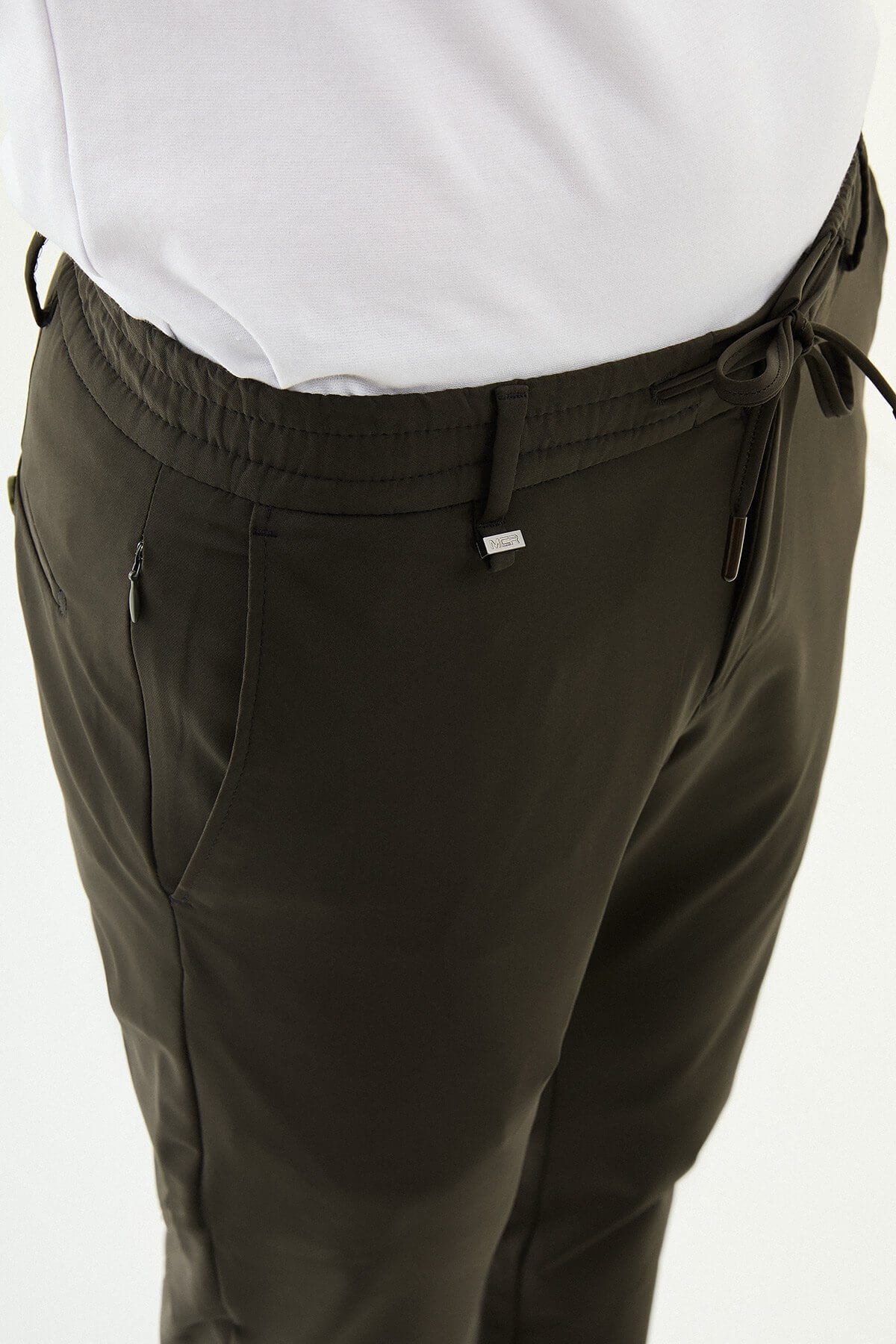 Man wearing olive green slim-fit summer trousers styled with a white polo shirt and casual sneakers.