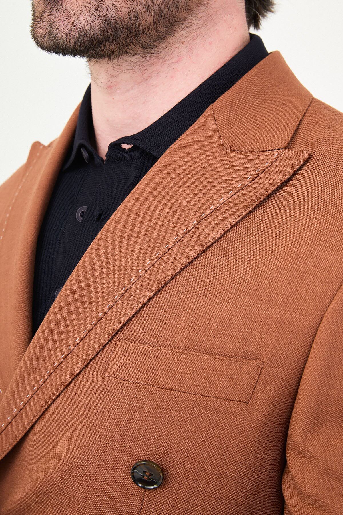 a Tile slim-fit double-breasted suit with peak lapels, contrast pick stitching, matching trousers, a black knit polo, and dark minimalist sneakers.
