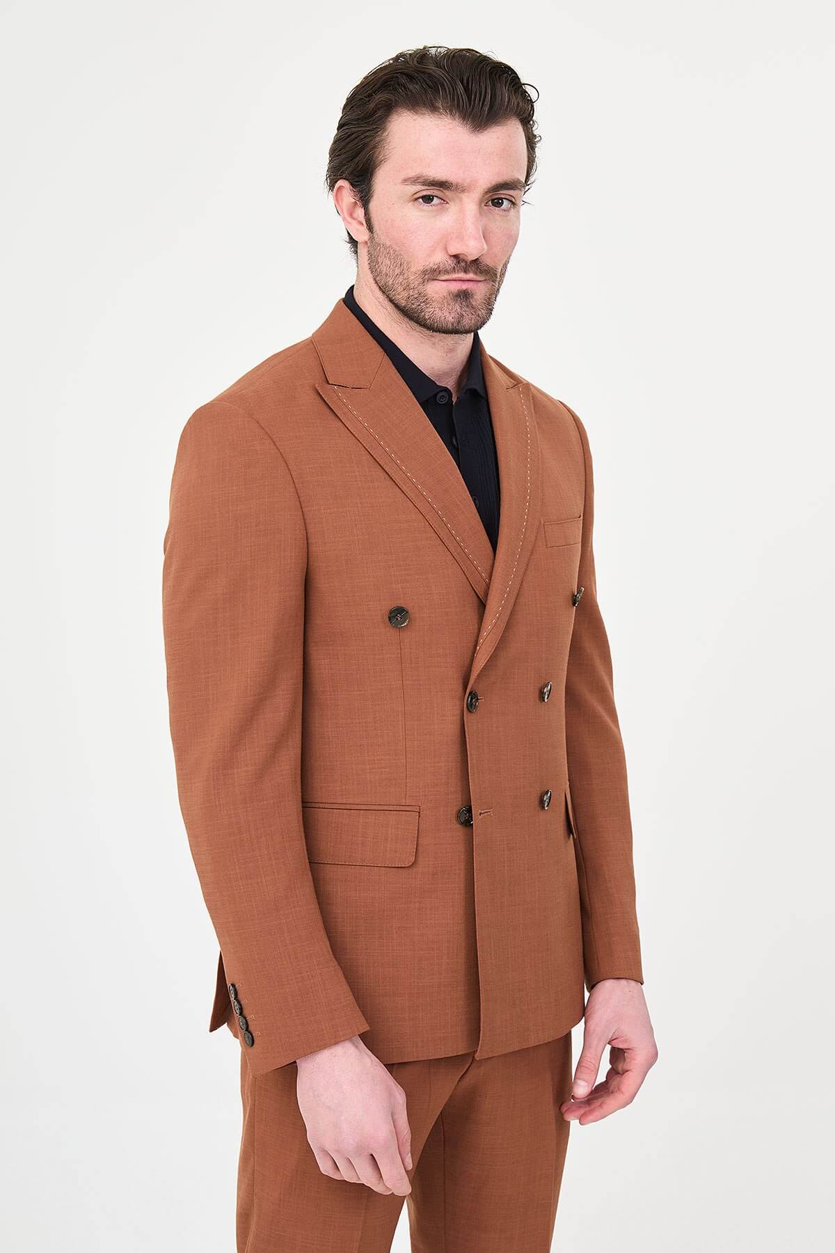 a Tile slim-fit double-breasted suit with peak lapels, contrast pick stitching, matching trousers, a black knit polo, and dark minimalist sneakers.