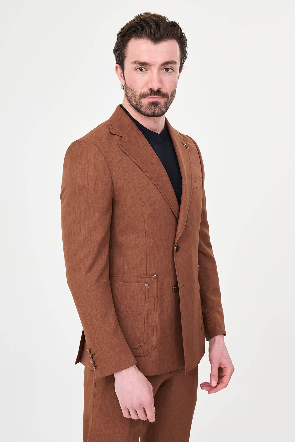 a tile slim-fit two-piece suit with notch lapels, utility-style stitched lower pockets, matching trousers, a black knit top, and brown leather shoes.