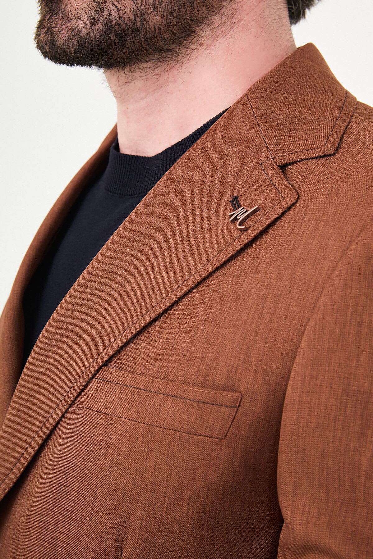a tile slim-fit two-piece suit with notch lapels, utility-style stitched lower pockets, matching trousers, a black knit top, and brown leather shoes.