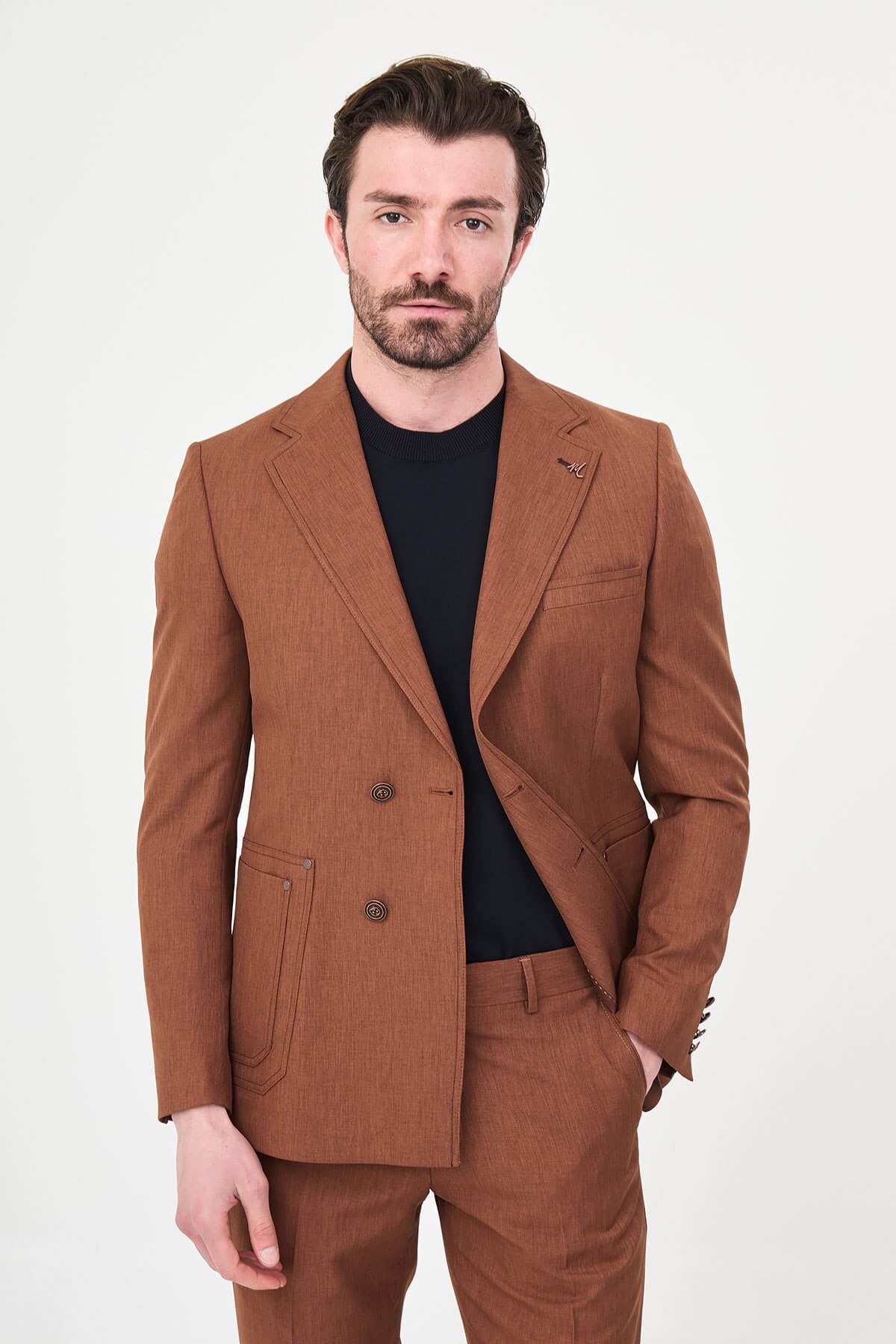 a tile slim-fit two-piece suit with notch lapels, utility-style stitched lower pockets, matching trousers, a black knit top, and brown leather shoes.