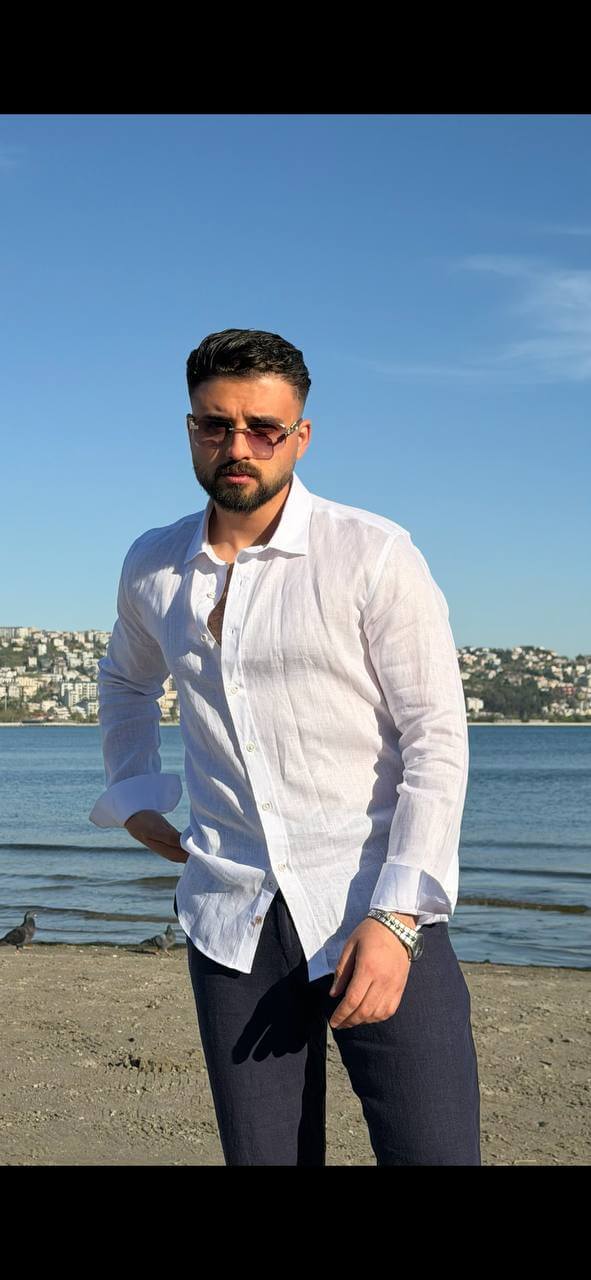 white linen collared dress shirt, standing by the water, sleeves rolled up, styled for summer.
