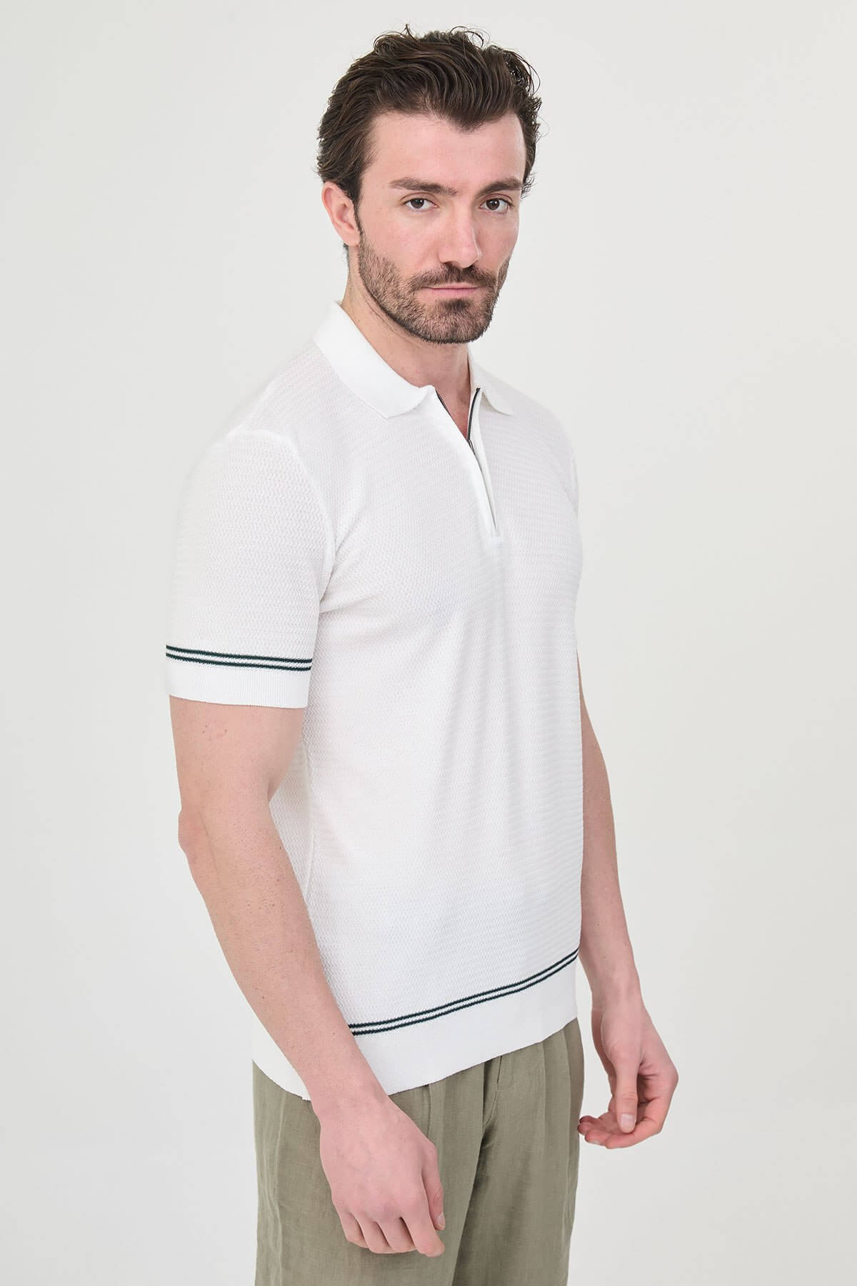 Man wearing white slim-fit quarter-zip polo t-shirt with dark stripe accents, styled with light brown trousers.