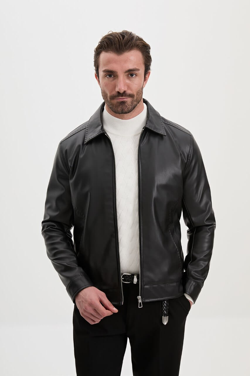 Men's black leather-look jacket styled with a cream knit sweater and black trousers.