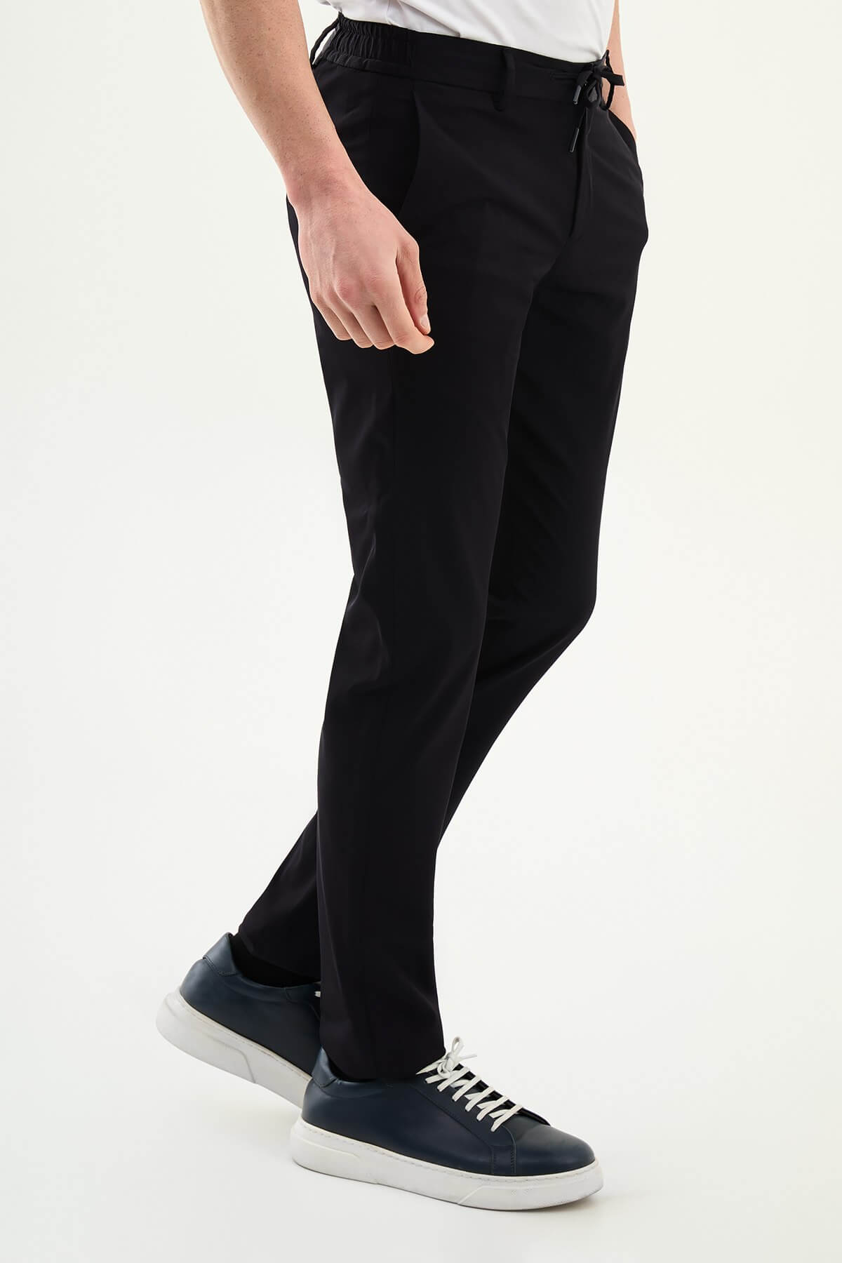 Man wearing navy blue slim-fit summer trousers styled with a white polo shirt and casual sneakers.