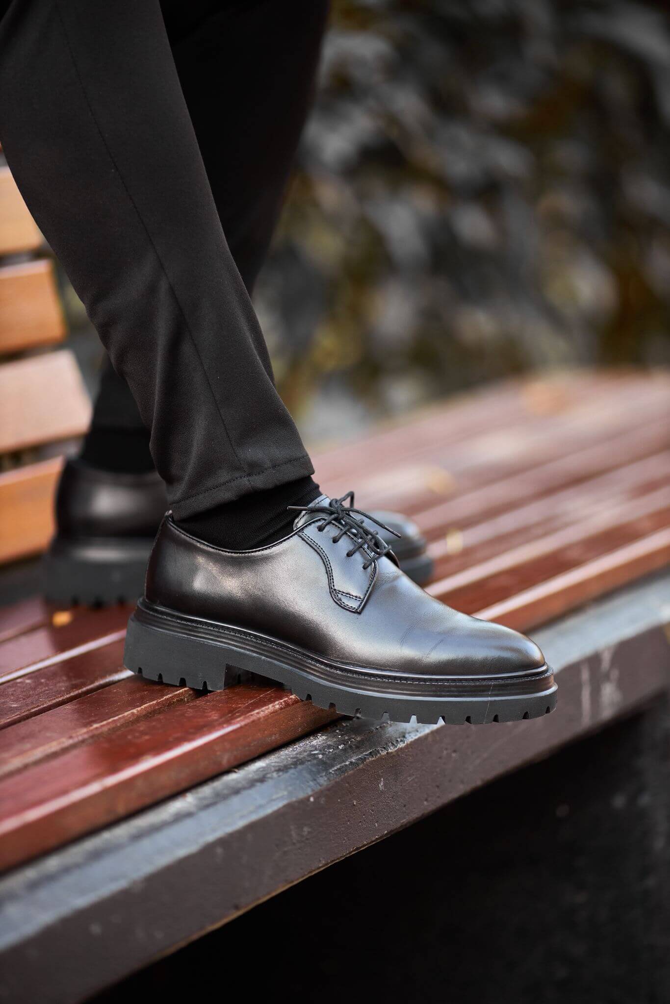 A man wearing black chunky-sole leather Derby shoes while walking down outdoor brick steps. 