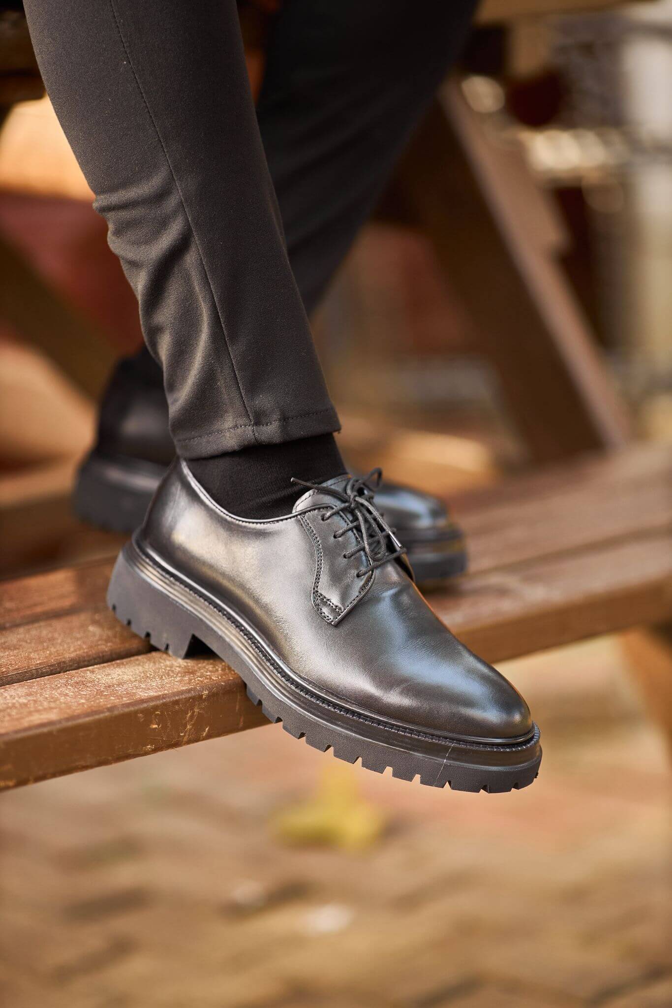  A man wearing black chunky-sole leather Derby shoes while walking down outdoor brick steps. 