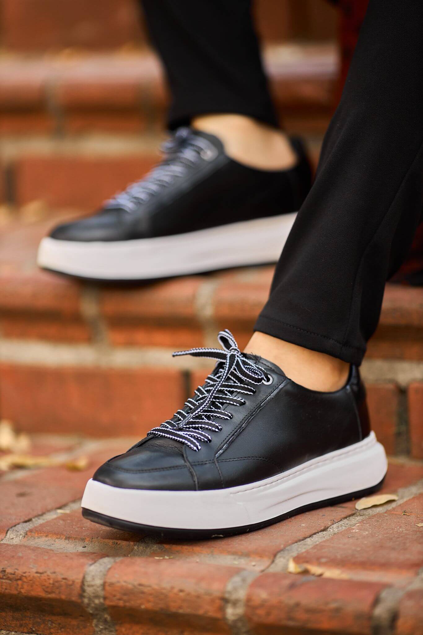 Black leather platform sneakers with white chunky sole on brick steps