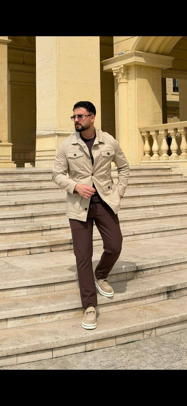 Men’s beige field jacket with multiple buttoned pockets, worn with brown trousers and a dark top, showcasing a casual outdoor look.