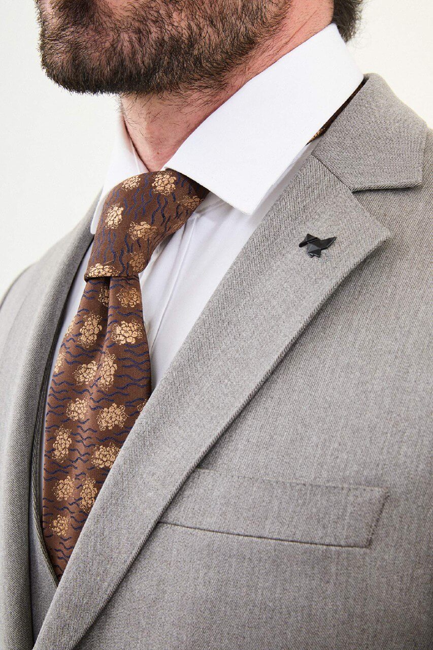 Men’s light gray slim-fit three-piece wool-blend winter suit with single-breasted jacket, notch lapels, matching waistcoat, dark buttons, and black origami lapel pin.