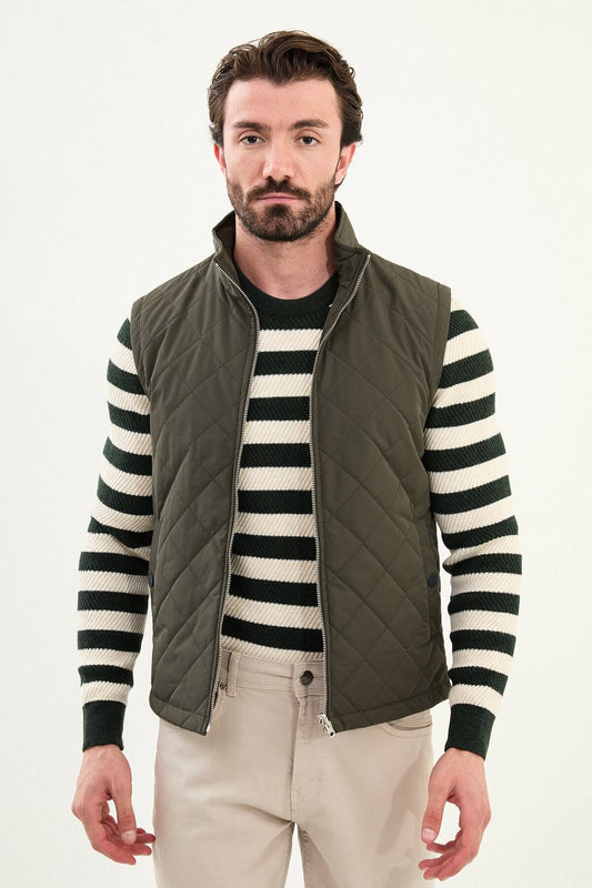 Men’s matte khaki/olive technical vest with a stand collar, zip front, and utility pockets, styled over a striped sweater for winter layering.