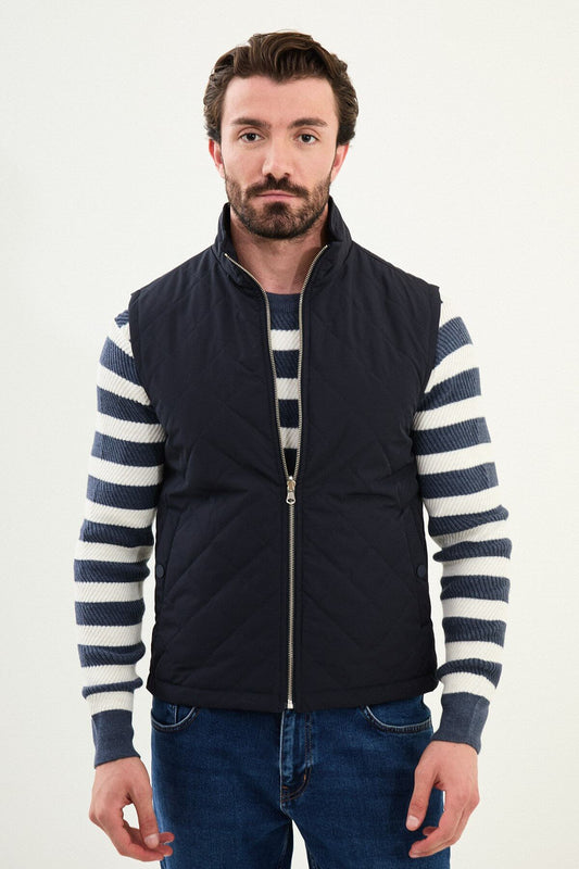 Men’s navy blue diamond-quilted technical vest with a matte finish, styled over a striped sweater for winter layering.