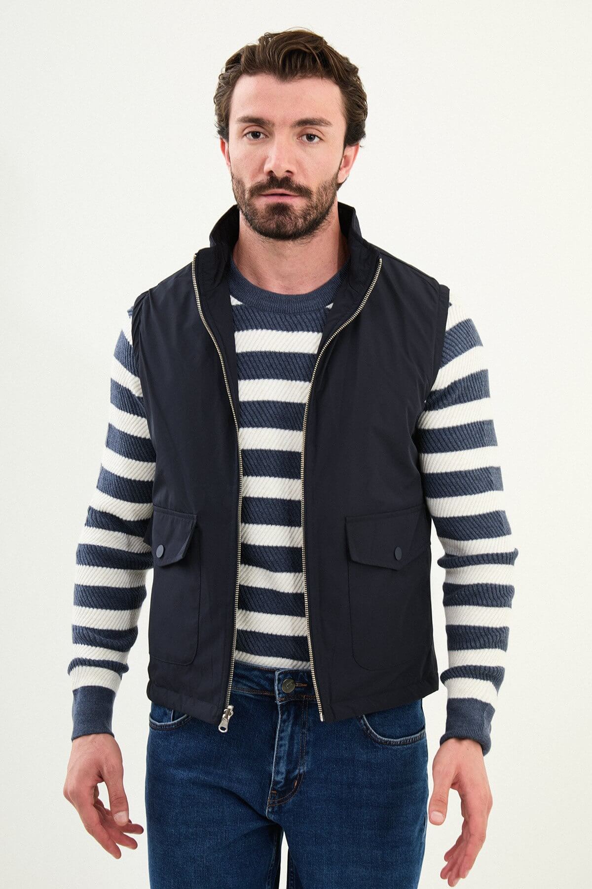 Men’s navy blue diamond-quilted technical vest with a matte finish, styled over a striped sweater for winter layering.