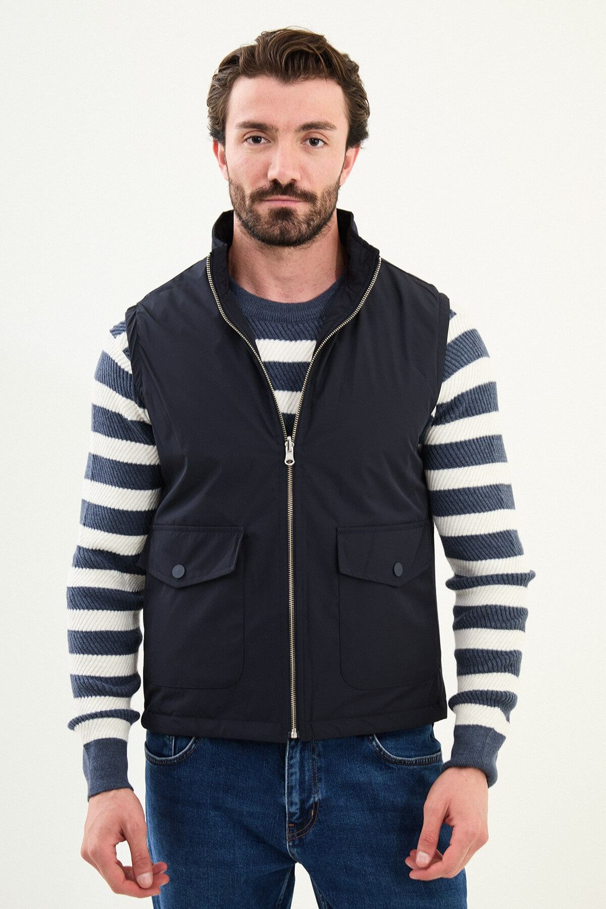Men’s navy blue diamond-quilted technical vest with a matte finish, styled over a striped sweater for winter layering.