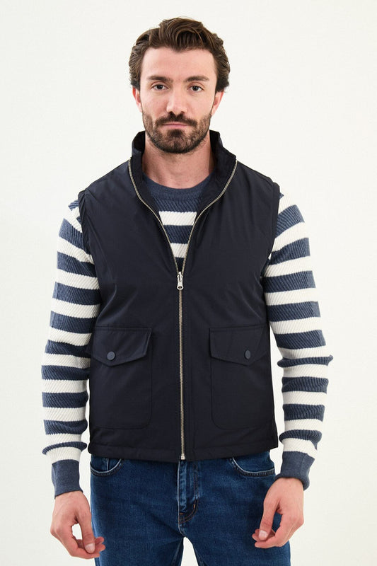 Men’s navy blue diamond-quilted technical vest with a matte finish, styled over a striped sweater for winter layering.