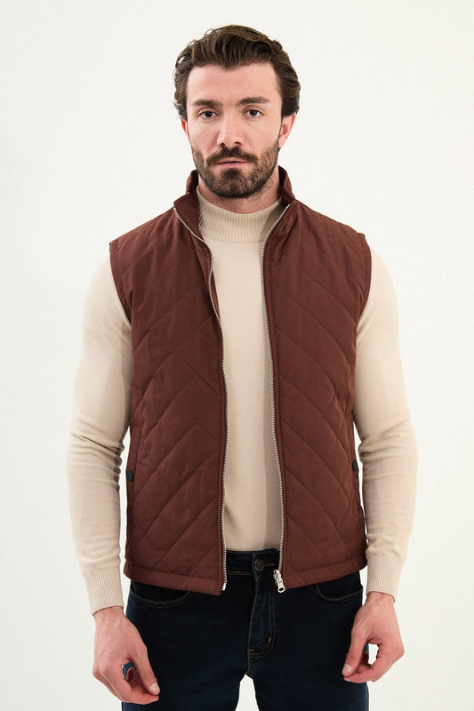 Tile rust diamond-quilted men’s technical vest in matte polyester, styled over a beige turtleneck with dark denim.