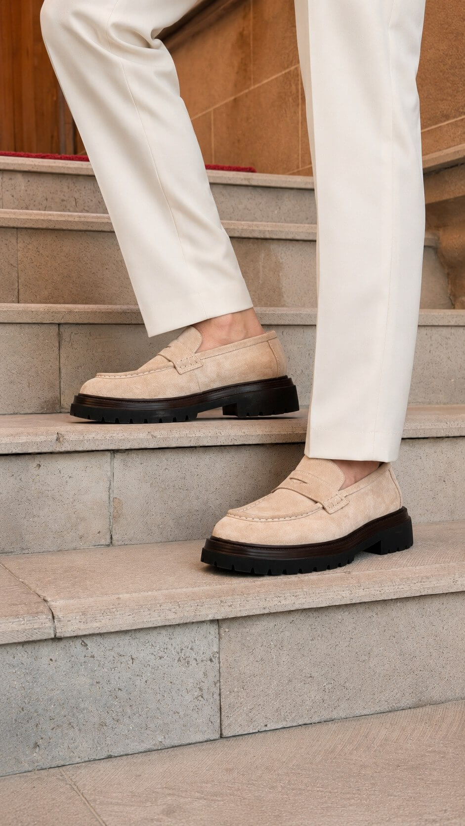 Men’s beige suede penny loafers with black lug sole styled with white trousers