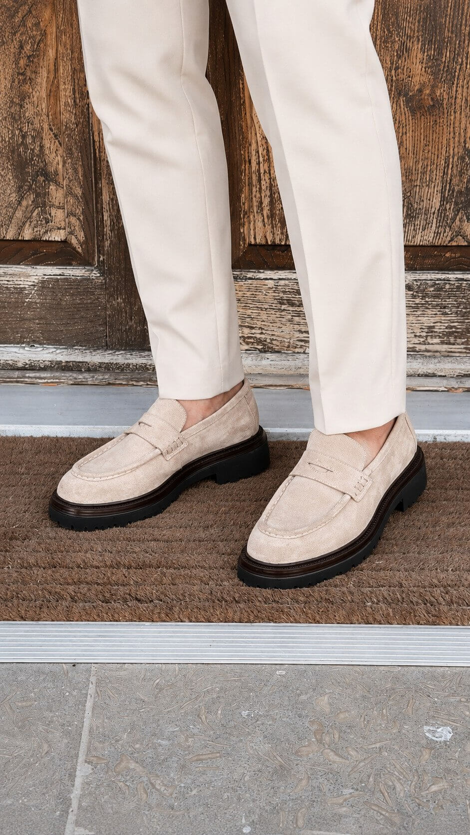 Men’s beige suede penny loafers with black lug sole styled with white trousers