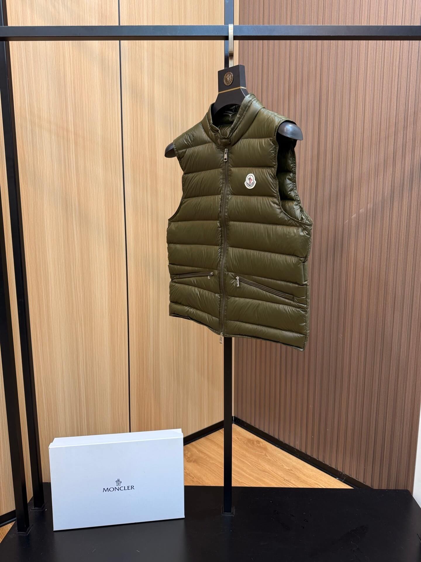 Green glossy down vest with chest logo patch and zippered pockets, Moncler Gui-inspired design.