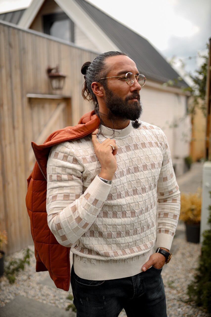 Man wearing a slim-fit beige knitwear sweater with geometric jacquard design, styled with dark jeans.