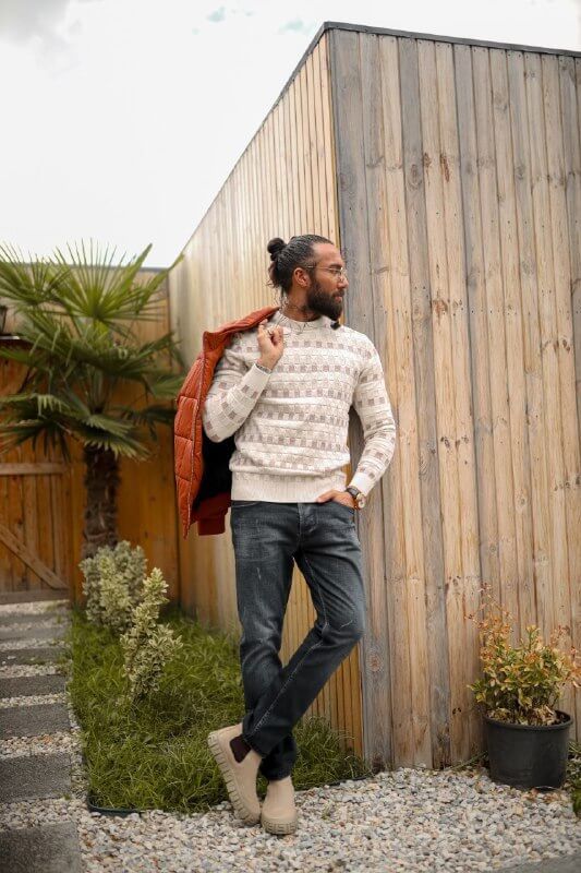 Man wearing a slim-fit beige knitwear sweater with geometric jacquard design, styled with dark jeans.