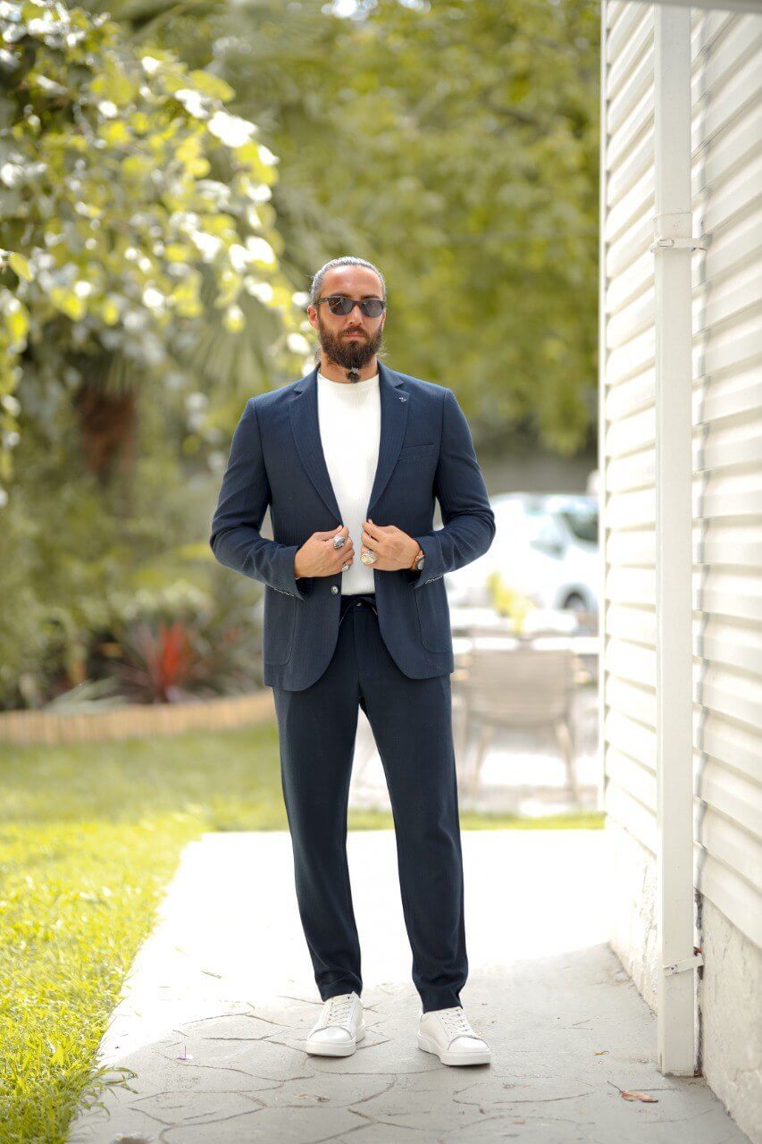 Man wearing a navy blue slim fit seersucker sports suit with a white crewneck top, styled with white sneakers in an outdoor setting.