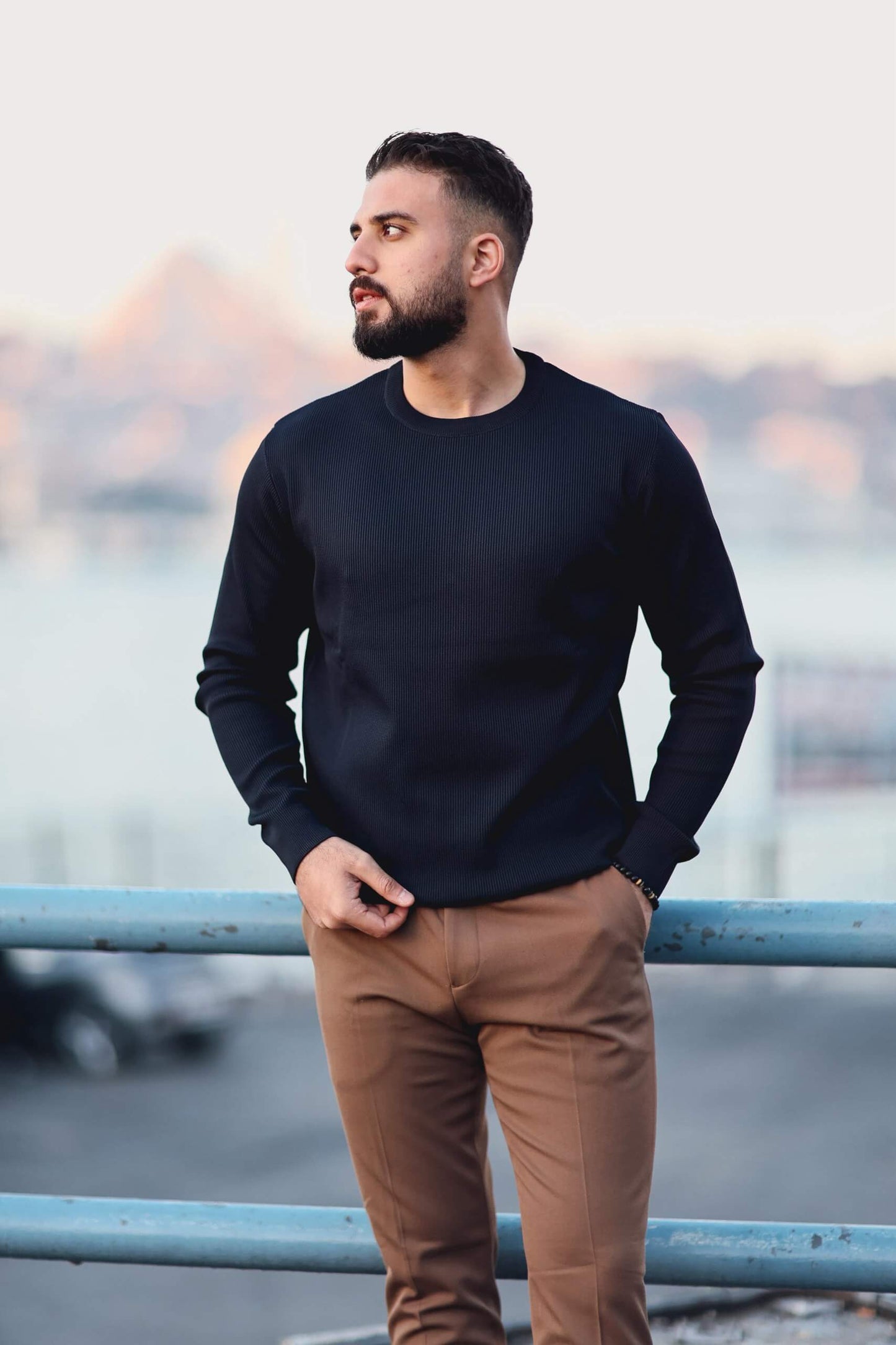 Men’s navy blue long-sleeve knit polo shirt worn outdoors, styled with camel slim-fit trousers