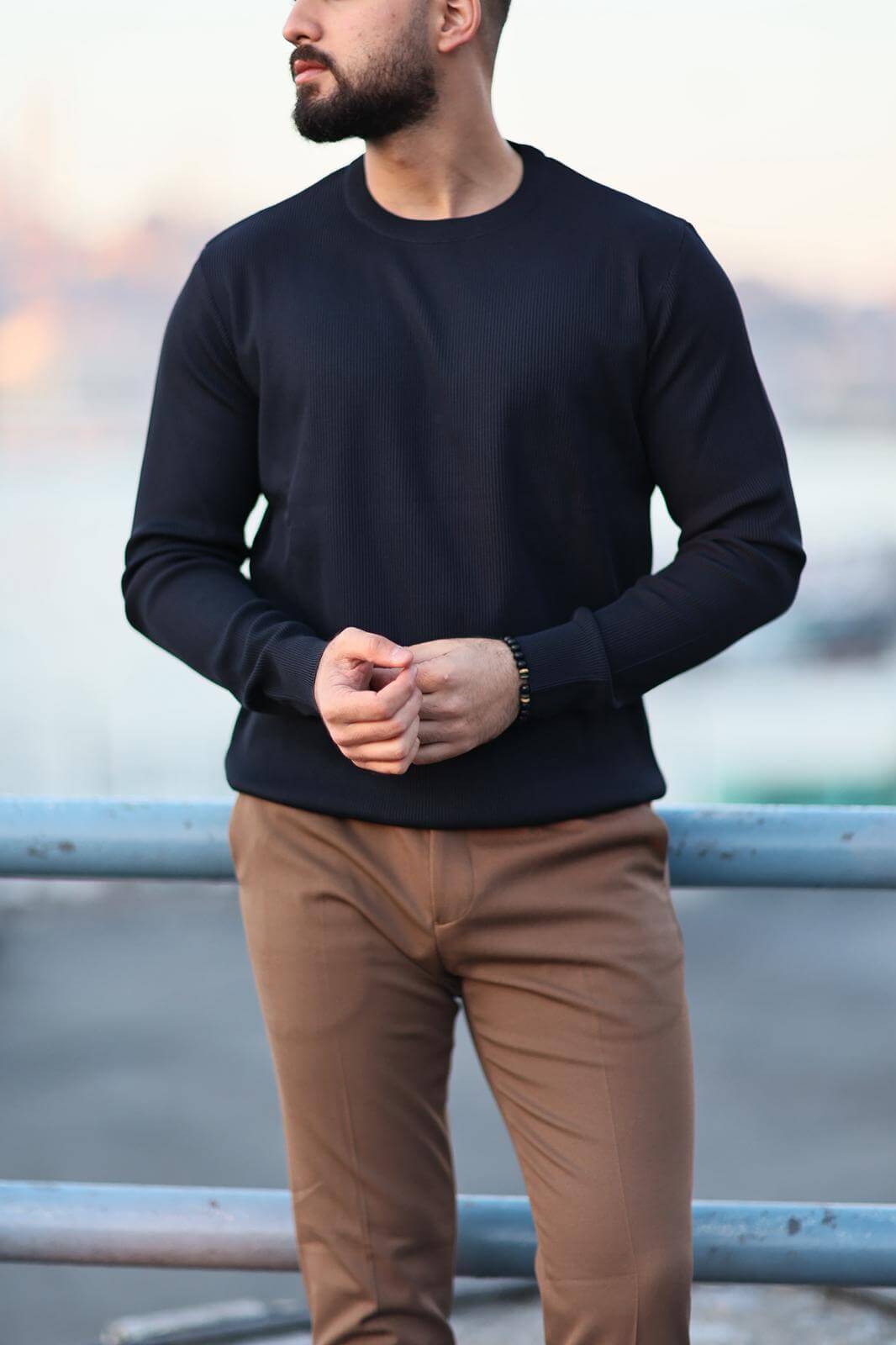 Men’s navy blue long-sleeve knit polo shirt worn outdoors, styled with camel slim-fit trousers