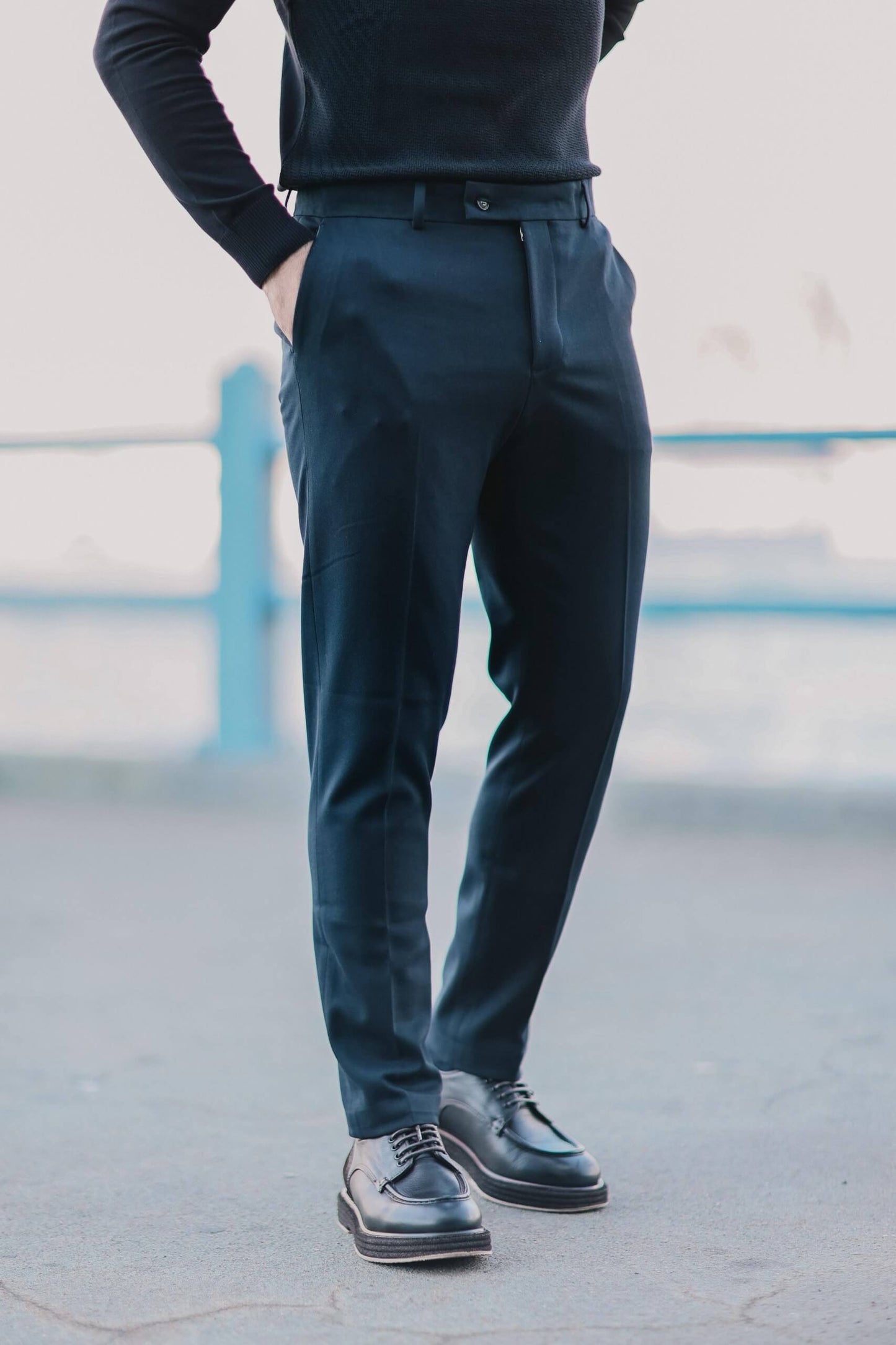 Men wearing navy blue slim-fit trousers paired with black derby shoes, standing outdoors in a clean minimalist urban setting.